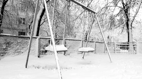 Φωτογραφικά πλάνα από άδειο χιόνι που καλύπτεται παιδική χαρά μετά από χιονοθύελλα. Δύο κούνιες κάτω από το χιόνι στο πάρκο — Φωτογραφία Αρχείου