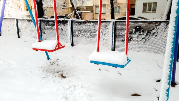 Zbliżenie strzał pokryte śniegiem plac zabaw. Dwa huśtawki pod śniegiem w parku — Zdjęcie stockowe