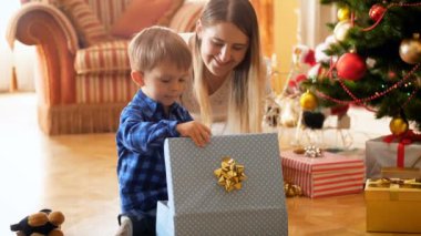 4k footage of little toddler boy sitting next to Christmas tree and packing toys in colroful boxes. Family giving and receiving presents on winter holidays and celebrations.