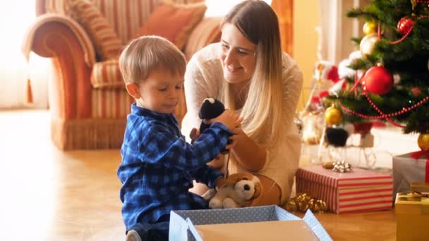 4k video de lindo niño pequeño con su madre embalaje de juguetes en cajas de regalo para dar regalos en Navidad. Dar y recibir regalos familiares en las vacaciones de invierno y celebraciones . — Vídeos de Stock