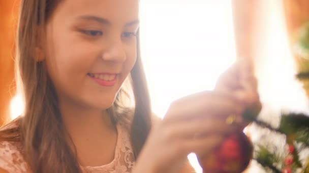 4k zaostřená portrét šťastné usmívající se mladé dívky, která visí na vánočním stromku s ozdobným balením. Rodinná dekorace na zimních prázdninách a oslavy. — Stock video