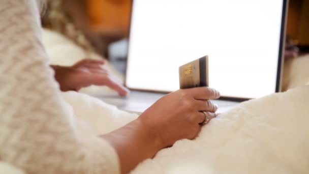 Κοντινά πλάνα βίντεο 4K της νεαρής γυναίκας που βρίσκεται στο κρεβάτι με φορητό υπολογιστή, κρατώντας πιστωτική κάρτα και περιήγηση στο ηλεκτρονικό κατάστημα. Λήψη concept για ηλεκτρονικές αγορές και ηλεκτρονικό εμπόριο. — Αρχείο Βίντεο