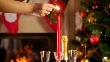 Yanan şömine ve parlayan Noel ağacı karşı kibrit ile mum yanan kadın el 4k görüntüleri. Yemek masası kış tatilleri ve kutlamaları büyük aile için servis.