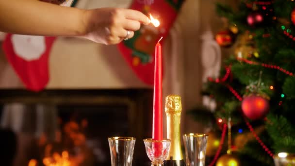 Imágenes de 4k de la mano femenina encendiendo velas con fósforos contra la chimenea ardiente y el brillante árbol de Navidad. Mesa de comedor servida para una gran familia en las vacaciones de invierno y celebraciones . — Vídeo de stock
