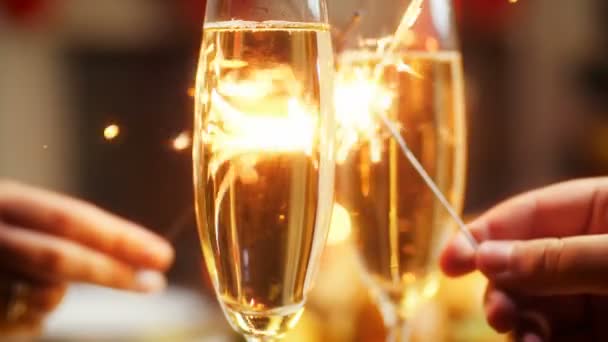CLoseup 4k metraje de hombre y mujer jóvenes enamorados sosteniendo dos bengalas ardientes en la mesa con copas de champán con gas. Familia celebrando Navidad y Año Nuevo — Vídeos de Stock