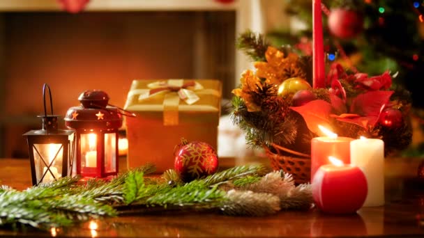 Imagens de close-up 4k queimando velas, decorações e presentes na mesa de madeira contra a árvore de Natal e lareira na sala de estar. Tiro perfeito para celebrações de inverno e feriados — Vídeo de Stock