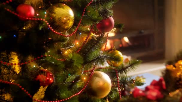 特写 4k 镜头美丽的五颜六色的发光灯， 花环和珠子在圣诞树上对燃烧火在客厅的壁炉.冬季庆典和假期的完美拍摄 — 图库视频影像