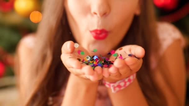 Closeup vídeo em câmera lenta de feliz sorrindo jovem soprando colorido de suas mãos na câmera. Tiro perfeito para festa, celebrações e feriados — Vídeo de Stock