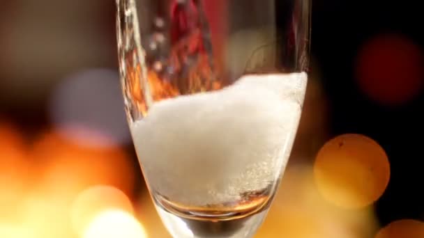 Macro slow motion video of pouring champagne from bottle in glass against glowing colorful lights. Gas bubbles and foam rising up. Perfect shot for parties,celebrations and holidays — Stock Video