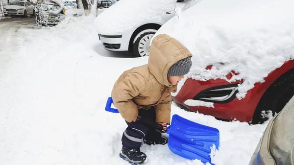 Shot of Boy hjälper till att städa upp och gräva upp den snötäckta bilen efter snöfall med stor blå spade — Stockfoto