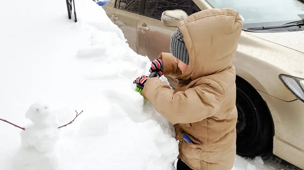 Bild av pojken städa upp snötäckt bil efter snön faller med stor borste. I den kalla vinter morgonen — Stockfoto