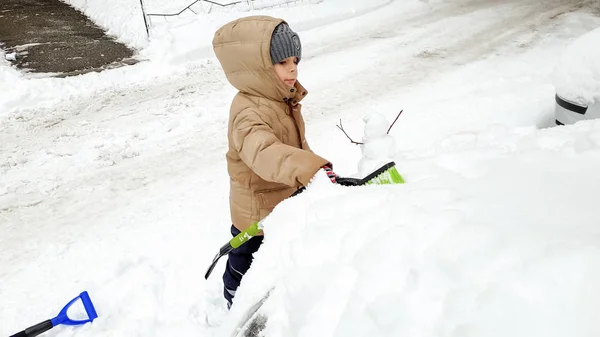 Zbliżenie portret szczęśliwego chłopca w marynarkę oczyścić śnieg pokryte samochód po burzy śnieżnej za pomocą wielkiego pędzla. W zimny śnieżny zimowy poranek — Zdjęcie stockowe