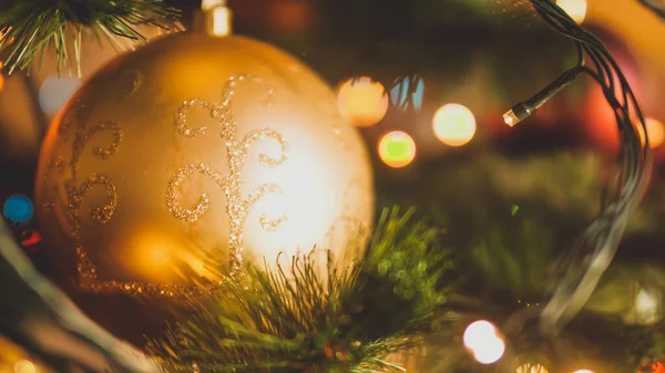 Closeup toned image of golden Christmas ball and glowing light garlands on Xmas tree — ストック写真