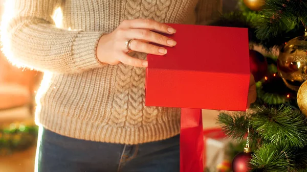 Closeup image of woman standing next to Christmas tree and opening red gift box — ストック写真