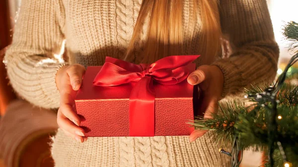Closeup image of young woman in sweater holding Christmas gift box with red ribbon — ストック写真