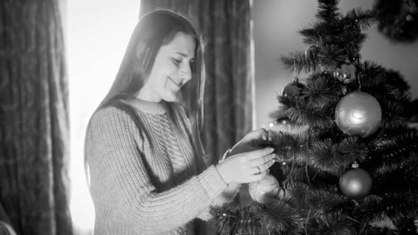 Black and white portrait of smiling young woman decorating Christmas tree at morning — Stock Photo, Image