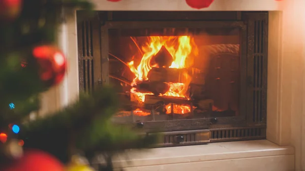 Detailní tónovaný obraz ohně plameny v krbu vedle zdobené vánoční stromeček v domě — Stock fotografie