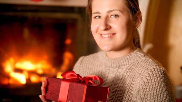 笑顔の幸せな女性の肖像画でザ · 暖炉のそばに座って、赤いギフトボックスを保持 — ストック写真