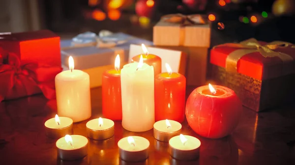 Detailní tónovaný obraz spousty hořících svíček proti barevné krabice s dárky na Vánoce a Nový rok — Stock fotografie