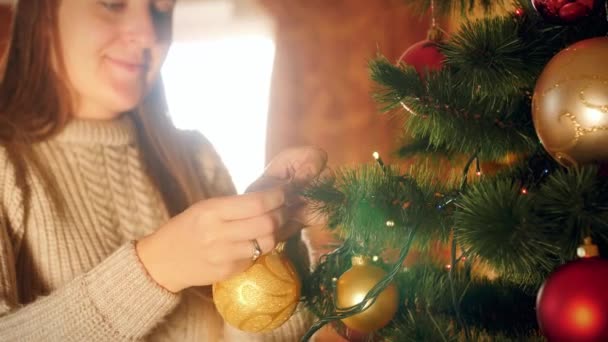 Hermosa joven sonriente poniendo bolas y bolas en el árbol de Navidad — Vídeos de Stock