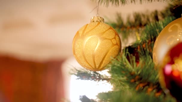 Gros plan vidéo 4k de boule étincelante dorée suspendue et filant sur l'arbre de Noël dans le salon 