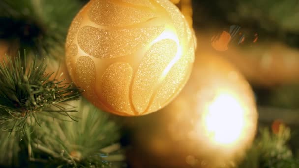 4k filmato di bauble d'oro appeso sull'albero di Natale contro luci colorate incandescenti — Video Stock