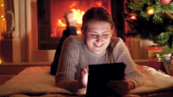 4kビデオの若い女性使用してタブレット上のクリスマスeve隣に燃える暖炉 — ストック動画