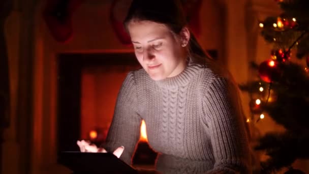 4k відео молодої жінки з цифровим планшетом, що сидить вночі поруч із яскравою ялинкою — стокове відео