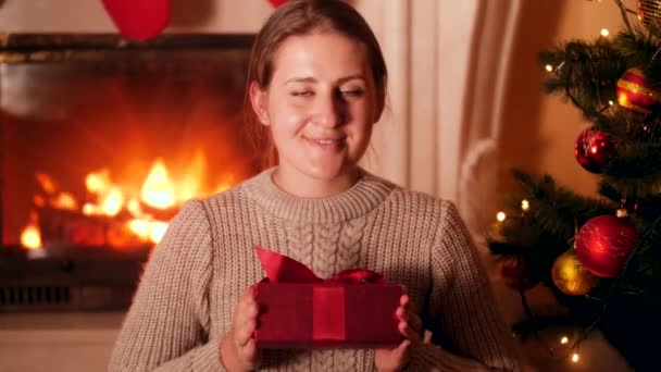 Retrato de una joven sonriente sentada en la sala de estar en la víspera de Navidad y mostrando el regalo de Santa en la cámara — Vídeos de Stock