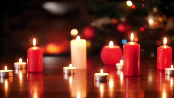 4k dolly vídeo of lots of burning red and white candles on wooden table against Christmas tree — Vídeo de Stock