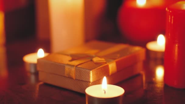 Closeup 4k filmagem de caixa de presente de ouro e velas em chamas na mesa de madeira à noite. Fundo perfeito ou pano de fundo para o Natal ou Ano Novo — Vídeo de Stock
