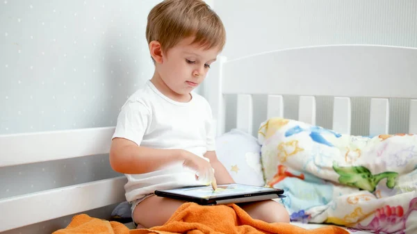 Lindo niño jugando juegos en la computadora tableta digital en la cama —  Fotos de Stock