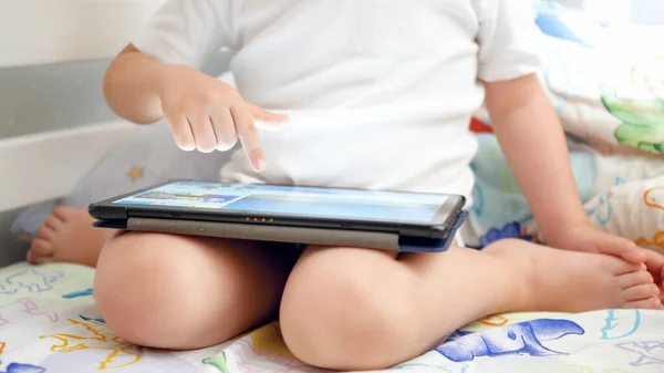 Imagen de primer plano de un niño pequeño sentado en la cama y usando una tableta digital —  Fotos de Stock