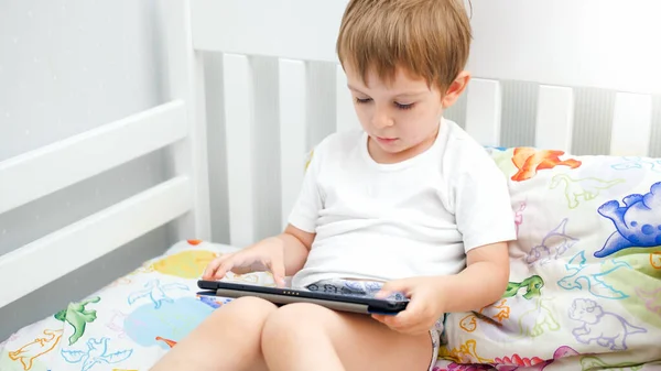 Potrait de niño pequeño acostado en la cama con tableta digital por la mañana —  Fotos de Stock