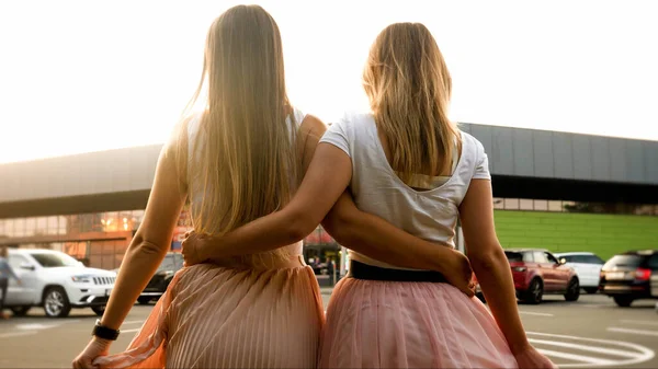 Immagine vista posteriore di due ragazze che si abbracciano e camminano sulla strada della città al tramonto — Foto Stock
