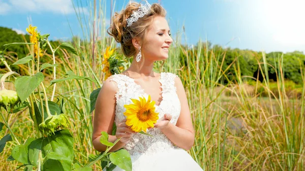 Portrait of beautiful smiling young bride with sunflower posing on field. — Stock Photo, Image