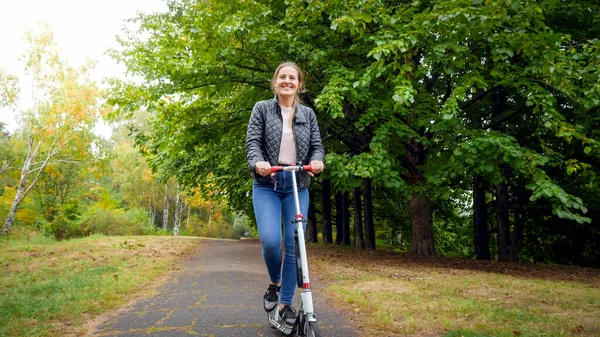 Jovem feliz montando em scooter sob grandes árvores no parque de outono — Fotografia de Stock