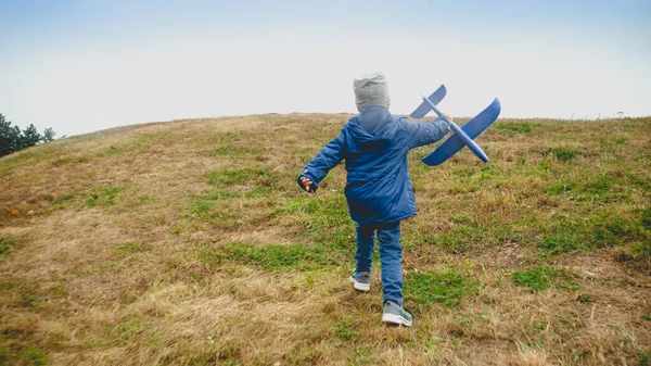 Σκηνή φωτογραφία του μικρού αγοριού με το παιχνίδι αεροπλάνο τρέχει στο λόφο στο πεδίο — Φωτογραφία Αρχείου
