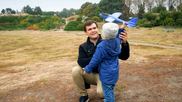 Retrato del joven padre sonriente enseñando a su pequeño hijo a lanzar un avión de juguete al campo —  Fotos de Stock