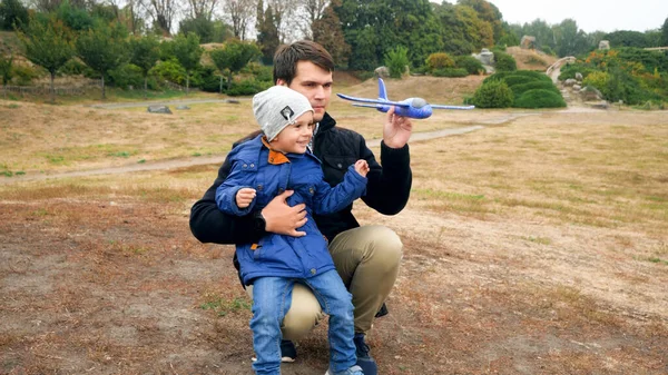 Malý usměvavý chlapec s mladým otcem hrající si s letadýlkem v poli — Stock fotografie