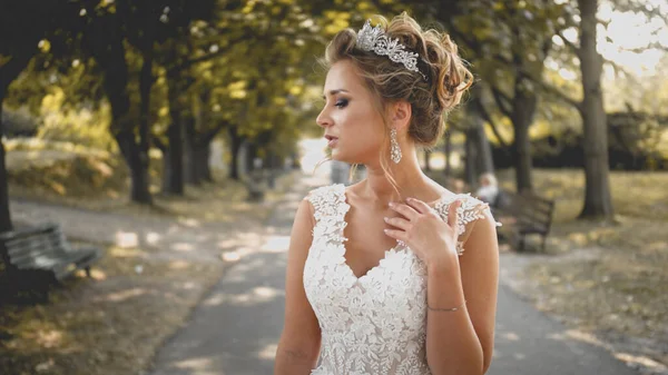 Retrato tonificado de novia rubia elegante en vestido blanco posando en callejón largo en el parque — Foto de Stock