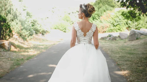 Visão traseira foto tonificada de noiva jovem sexy em vestido de casamento longo andando no parque — Fotografia de Stock
