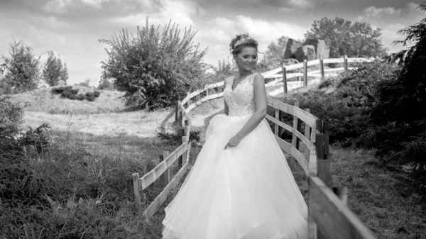 Zwart-wit portret van een mooie glimlachende jonge bruid poserend bij een lang houten hek op de boerderij — Stockfoto