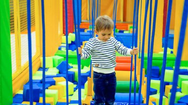 Küçük konsantre çocuk alışveriş merkezindeki çocuk oyun odasında ipler ve köprüler üzerinde dengede duruyor.