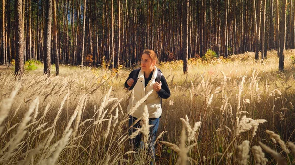 Toned portrait of beautiful young woman with backpack walking through high grass in forest — Stock Photo, Image