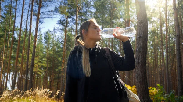 Portrait of beautiful tourist having a break and drinking water from plastic bottle in forest — Stok Foto