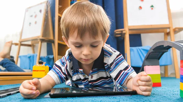 Portret 4-letniego chłopca leżącego na dywanie w swoim pokoju i korzystającego z komputera z tabletem cyfrowym — Zdjęcie stockowe