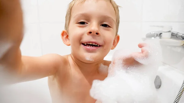 Retrato de niño sonriente feliz bañándose con espuma de jabón mirando en la cámara — Foto de Stock