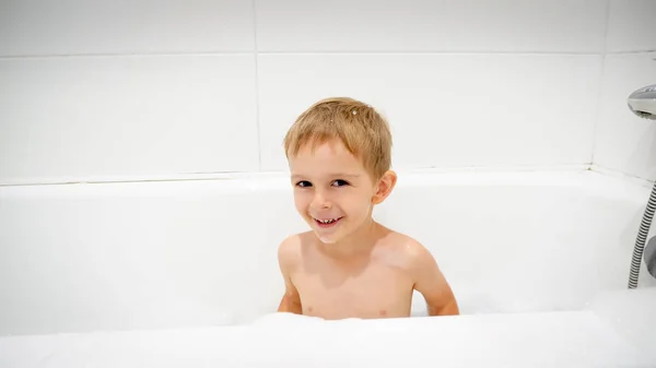 Retrato de lindo niño sonriente sentado en el baño lleno de espuma de jabón — Foto de Stock