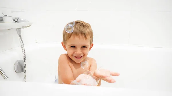 Retrato de niño risueño alegre lavándose en el baño y jabón burbujas cathing en la mano — Foto de Stock